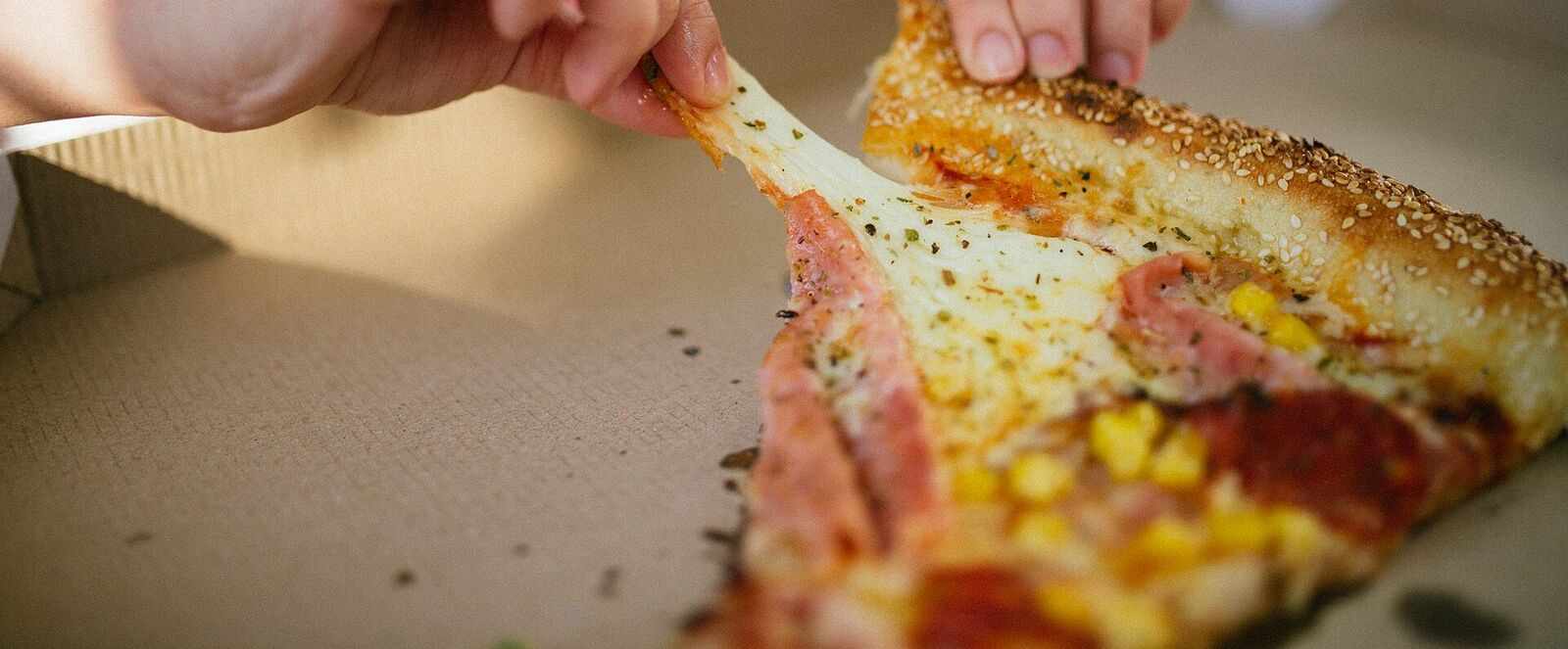 A kid's hands pulling a cheesy slice out of a pizza box