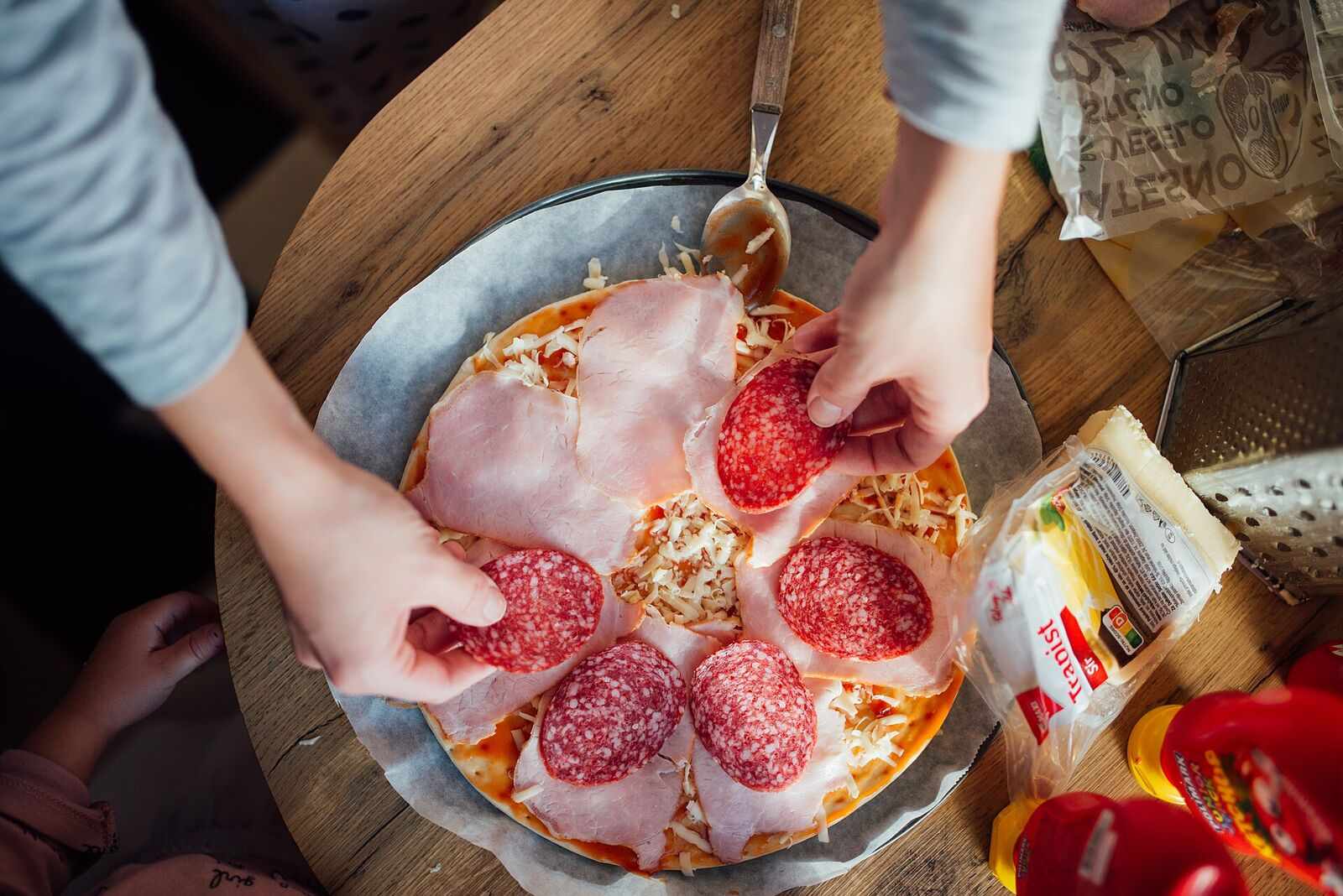 Hands placing pepperoni onto a pizza before it goes in the oven